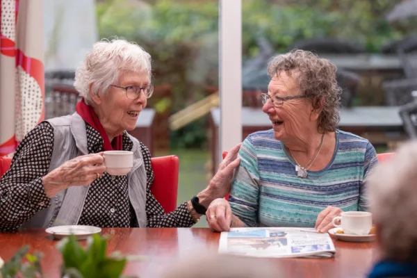 Bewoners lachen naar elkaar aan tafel - Dagbesteding