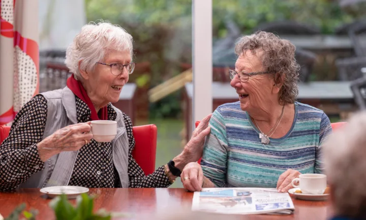 Bewoners lachen naar elkaar aan tafel - Dagbesteding